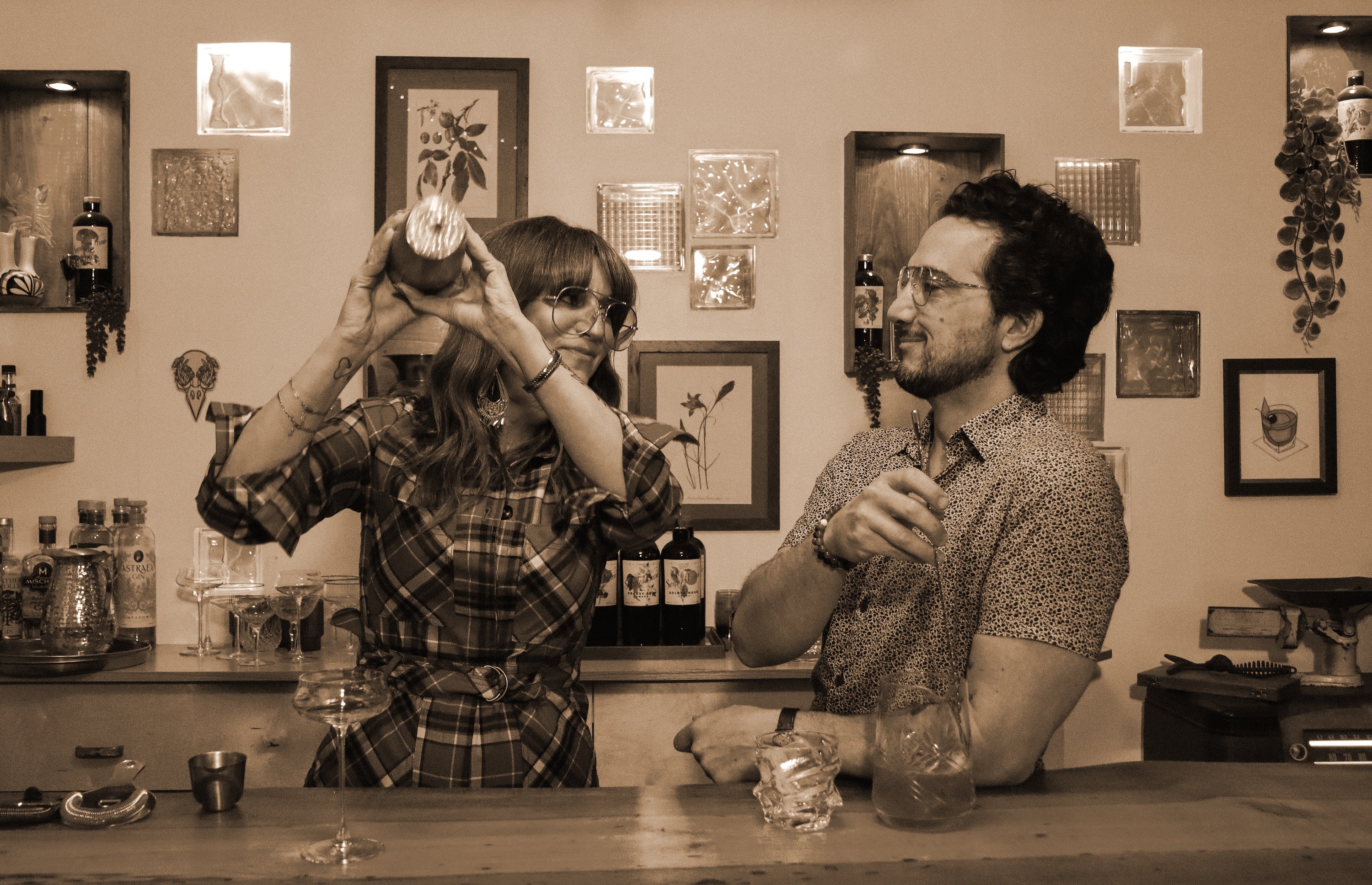SennzaFinne at a bar counter with drinks, surrounded by framed pictures on the wall.